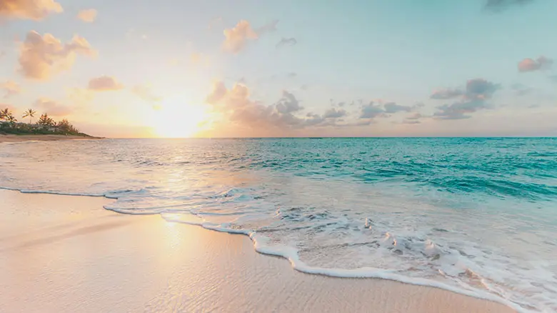 Sandy beach with gentle waves and clear blue water under a bright sky.