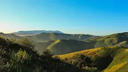 Scenic hill landscape with rolling slopes covered in grass or vegetation under a clear sky.