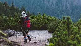 Person hiking or trekking on a trail surrounded by nature, carrying a backpack and enjoying the outdoors.