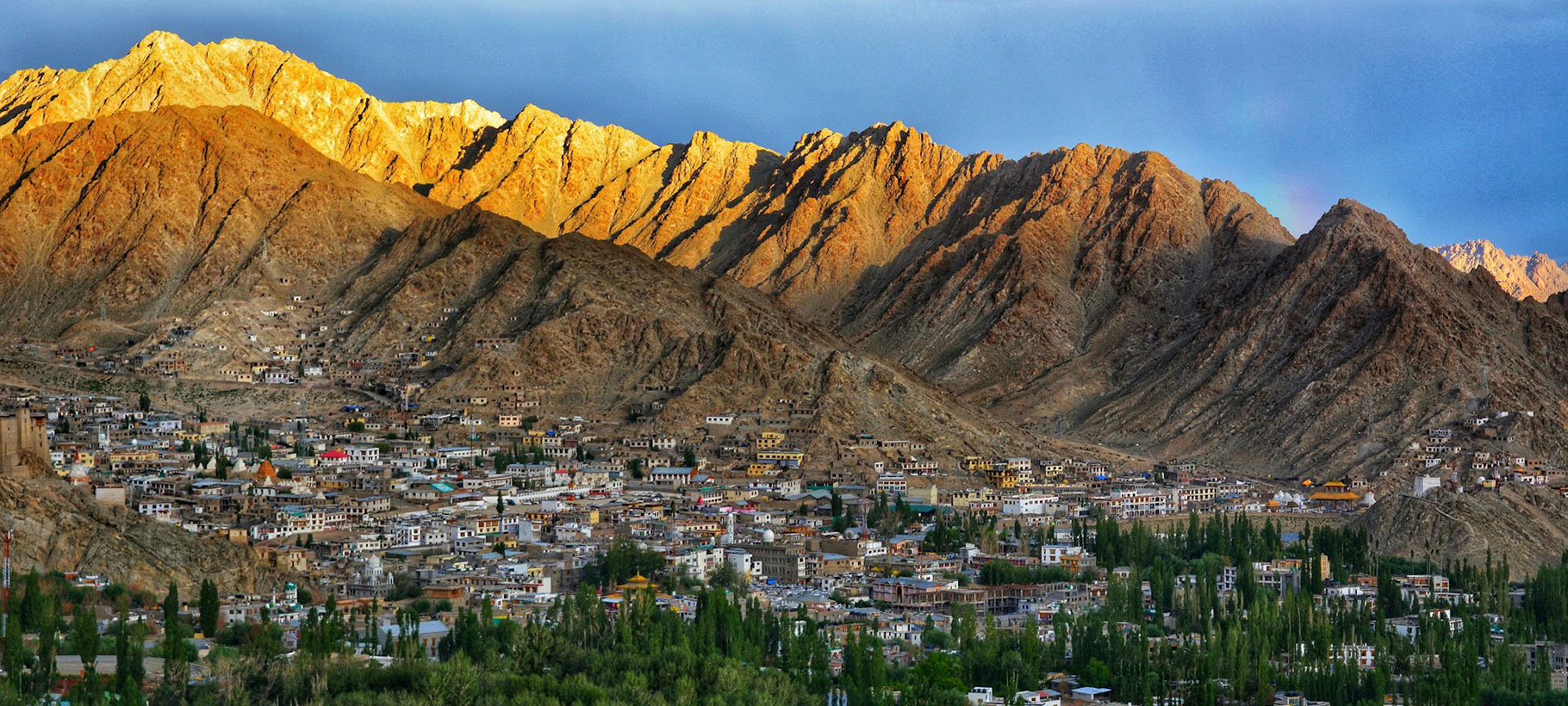 Scenic view of Leh, Ladakh, with rugged mountains, traditional Tibetan-style buildings, and clear blue skies.