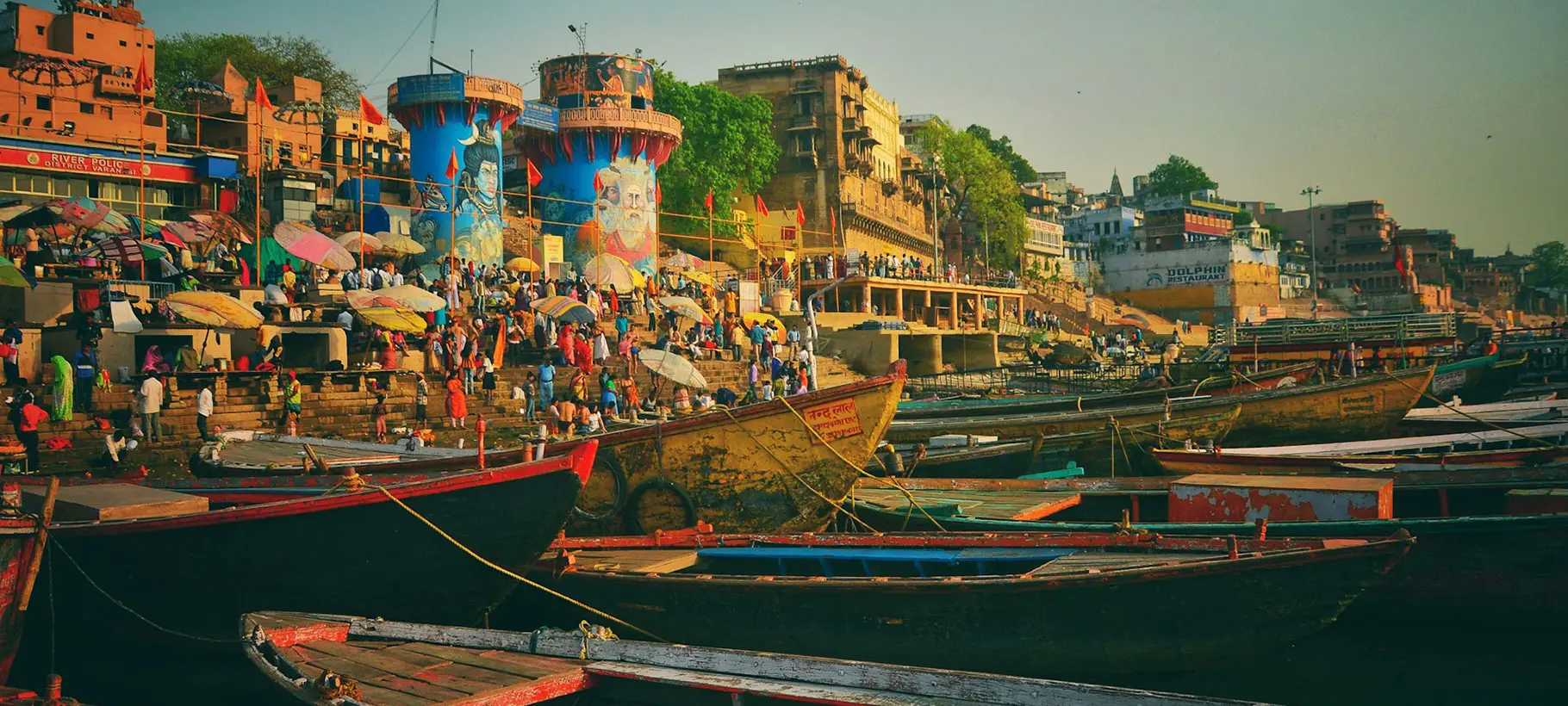 The sacred city of Varanasi, with ghats along the Ganges River, where pilgrims perform rituals and boats float on the water.